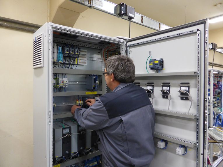 Eine Person arbeitet an einem offenen Schaltschrank mit verschiedenen elektrischen Komponenten und Steuerungen. Sie steht seitlich und fokussiert sich auf die interne Verdrahtung im Gerät.